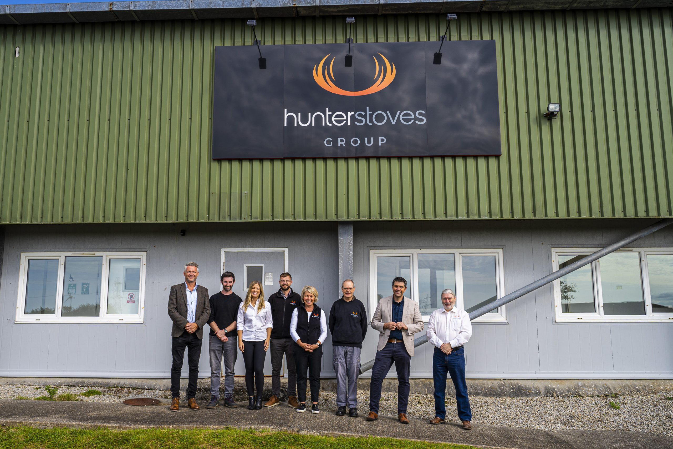 Hunter Stoves team posing with Scott Mann MP and Andy Hill from the SIA during their visit to the Camelford Factory, standing in front of Hunter Stoves UK Production Facility